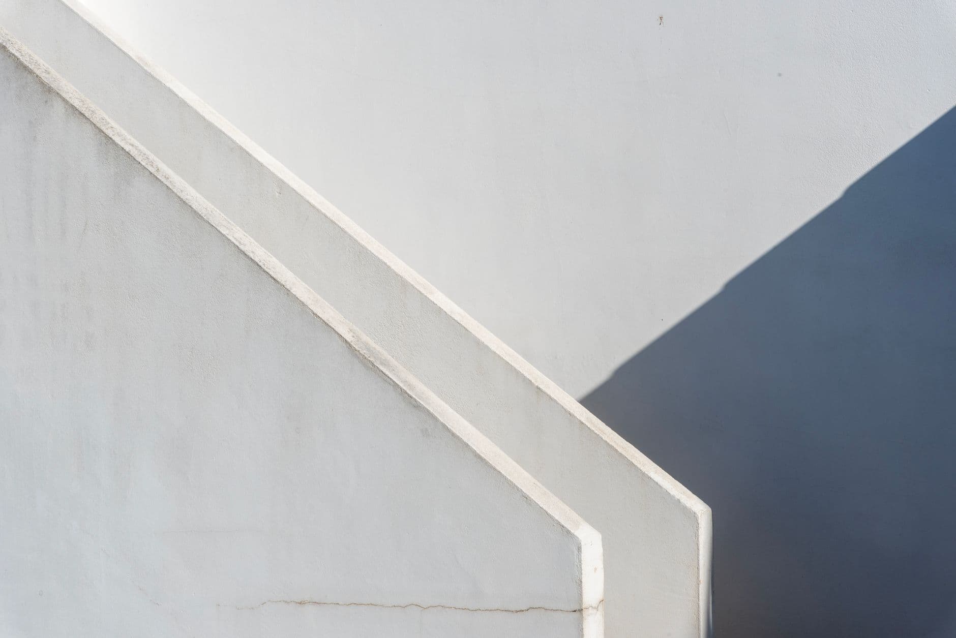 Diagonal parapet of a white exterior staircase with a hard shadow falling across the wall behind it.