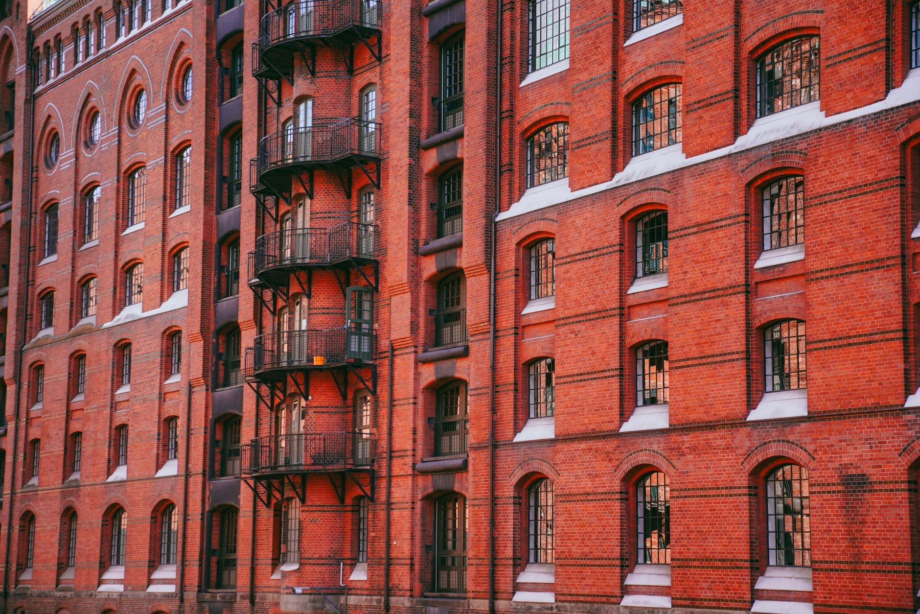 Red brick warehouse facades in Hamburg's Speicherstadt district, with rows of arched windows and black iron balconies stepping into the distance.