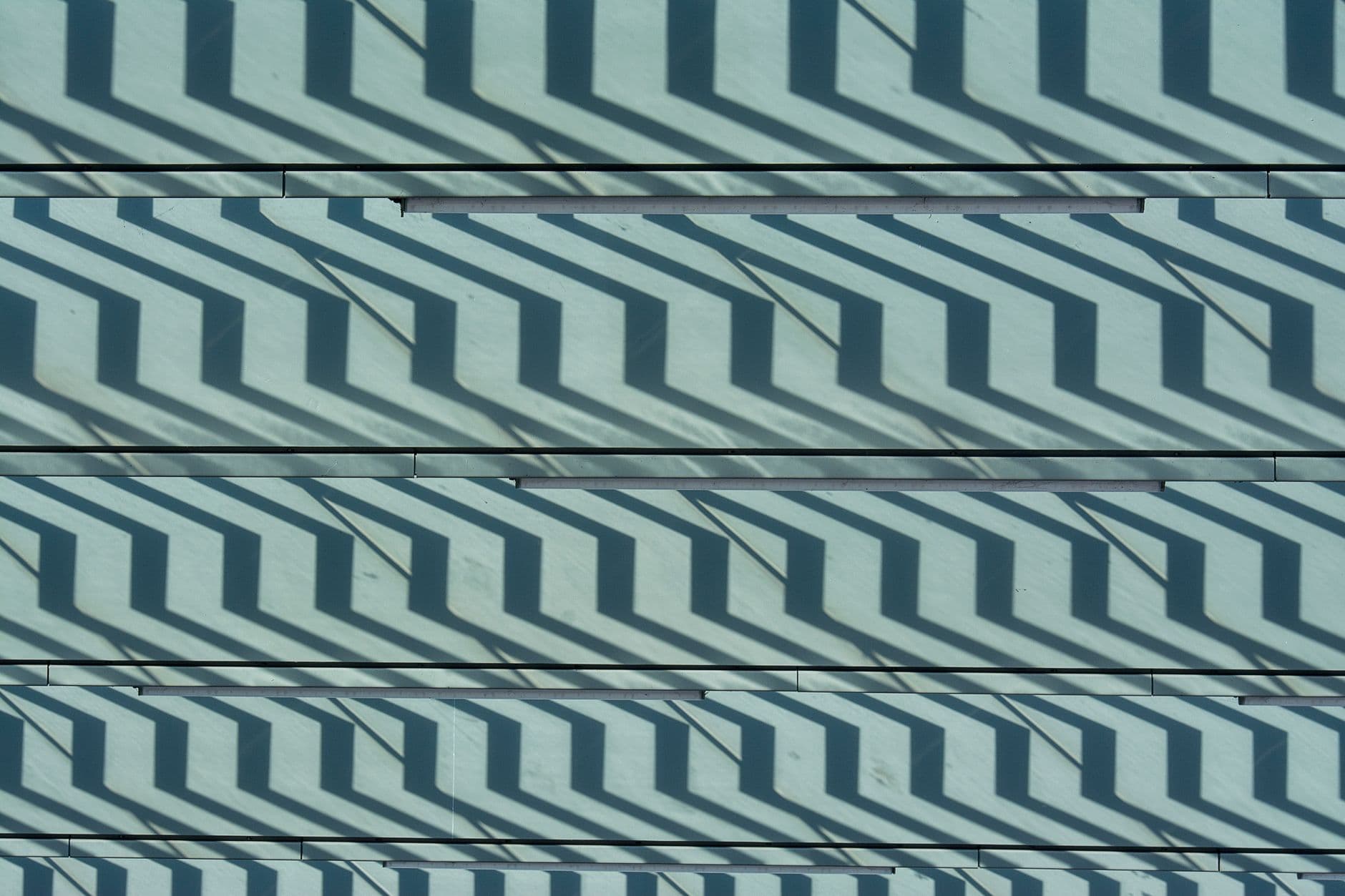 Zigzag shadows from a railing repeating across pale cladding panels in even horizontal bands.